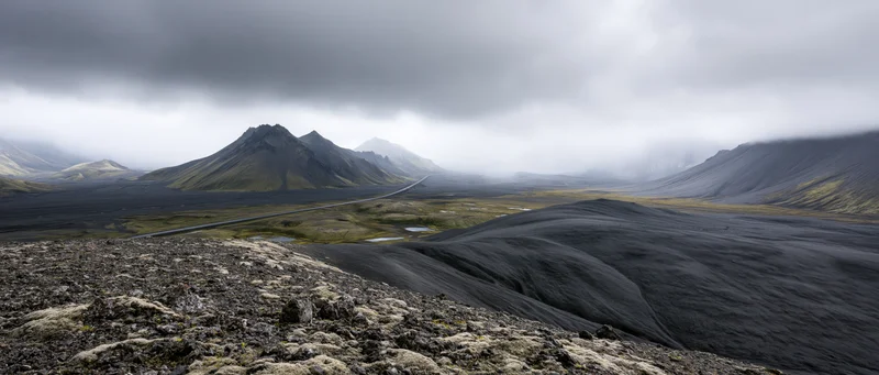 Volcanic landscape with black lava fields and winding road through misty highlands in Iceland