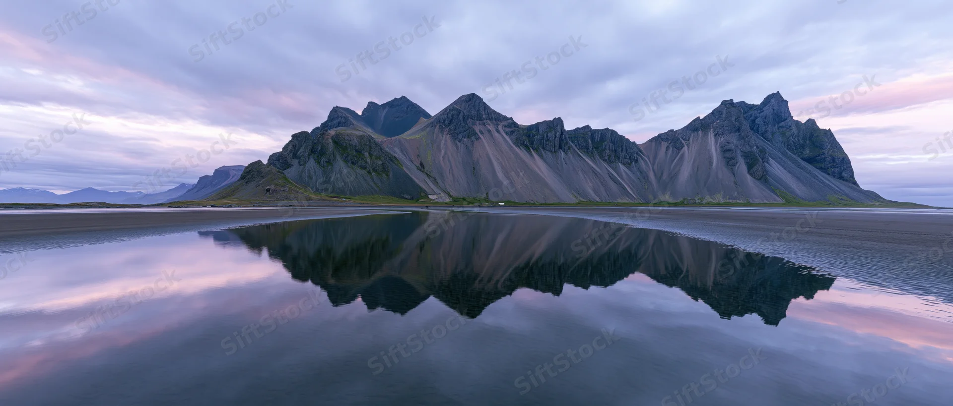 Rugged mountain range reflected in still water at twilight along a coastal shore