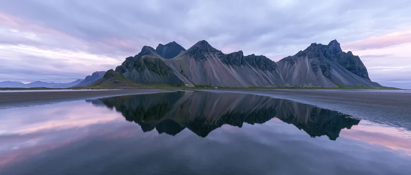 Rugged mountain range reflected in still water at twilight along a coastal shore