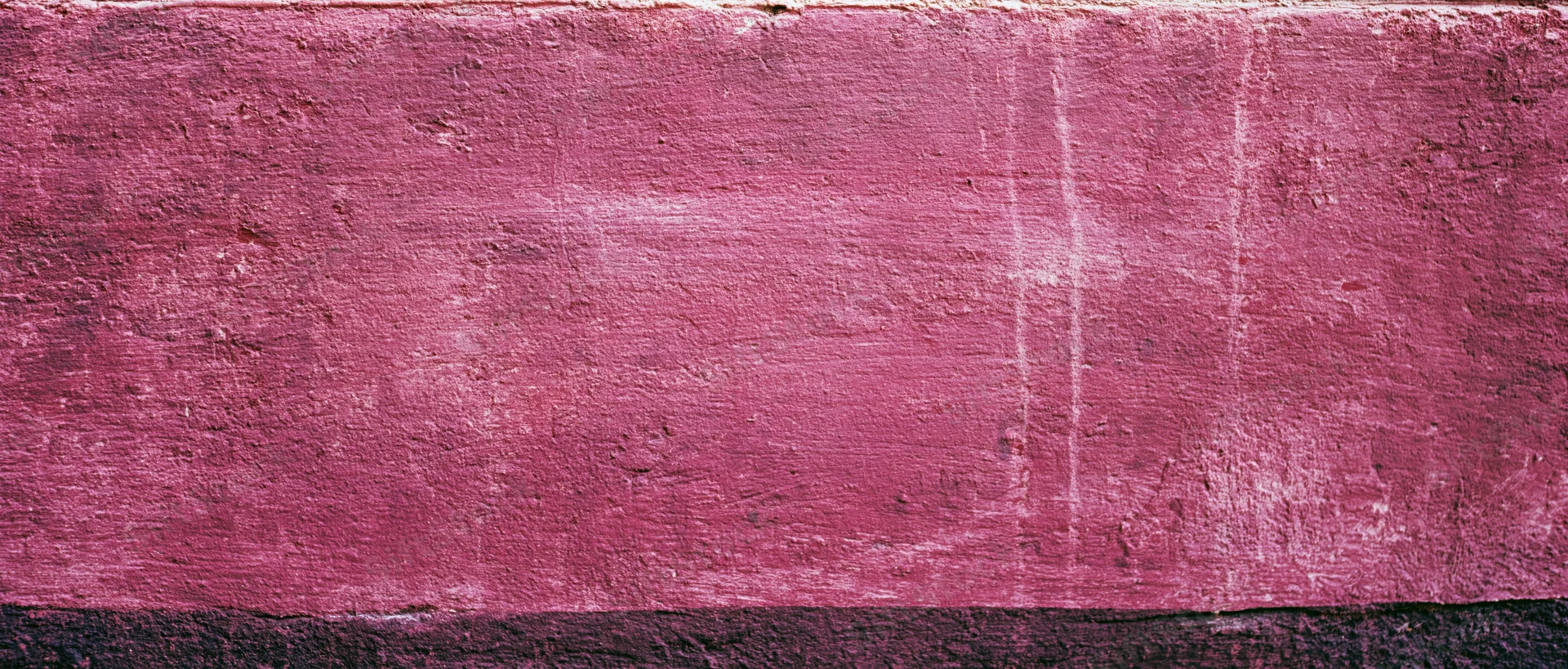 Textured pink painted wall with weathered surface and dark baseboard