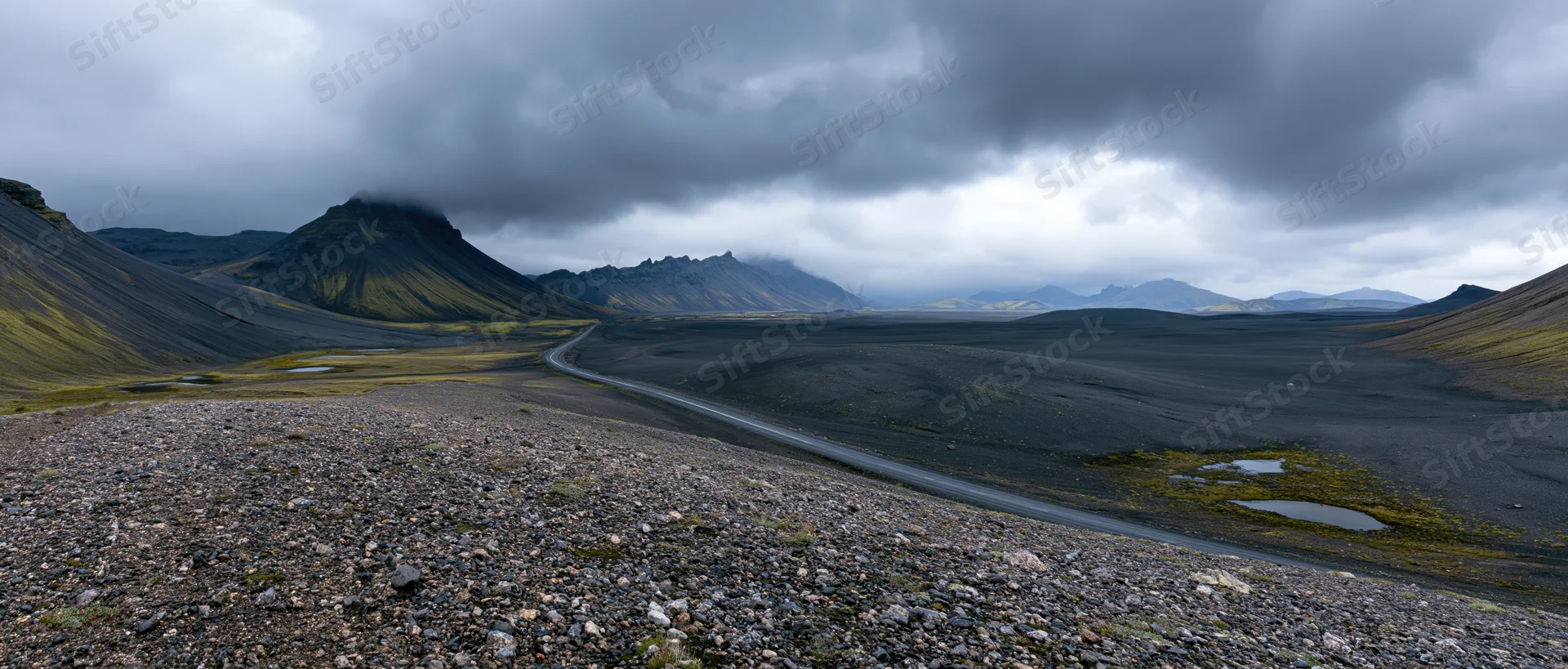Winding road through volcanic landscape with black lava fields and misty mountains under overcast sky