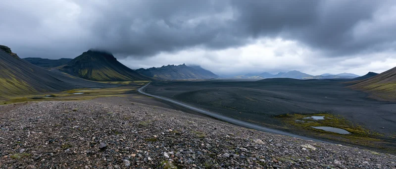 Winding road through volcanic landscape with black lava fields and misty mountains under overcast sky