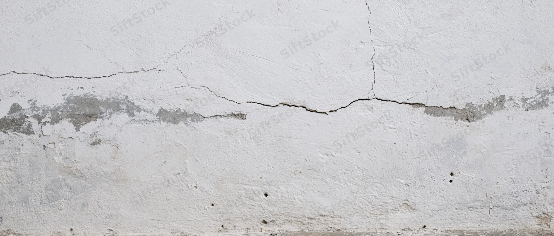 Cracked white plaster wall showing structural damage and foundation issues