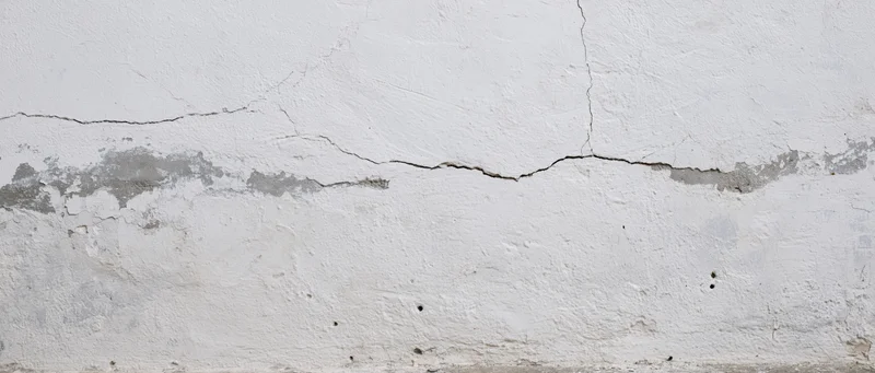 Cracked white plaster wall showing structural damage and foundation issues