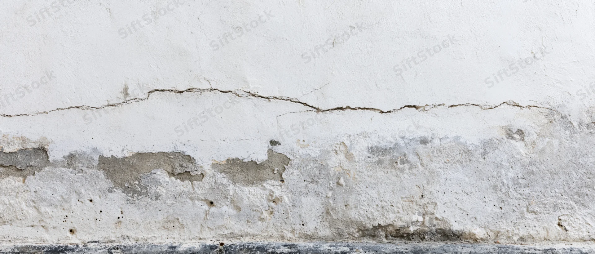 Cracked white plaster wall showing structural damage at base near floor
