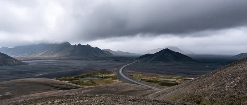 Winding road through volcanic black lava field under overcast sky in Iceland