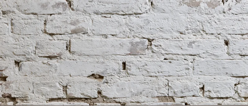 White painted brick wall with visible mortar and cracks, showing aged texture and rustic character