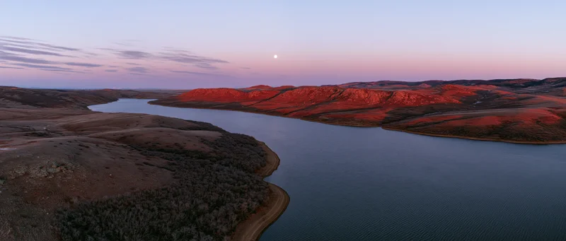 Aerial view of a winding river through red rock hills at sunset