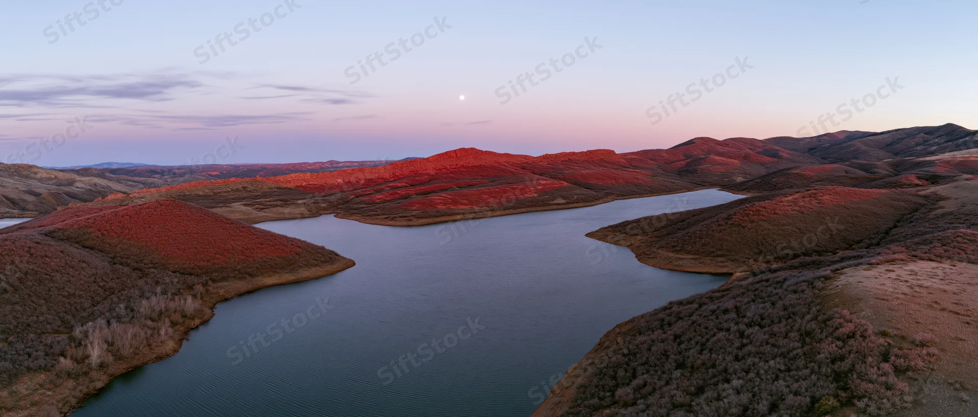 Aerial view of a calm lake surrounded by red-hued hills at sunset