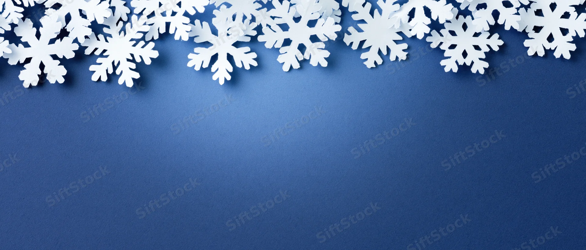 White paper snowflakes arranged in a border along the top of a blue background with copyspace below