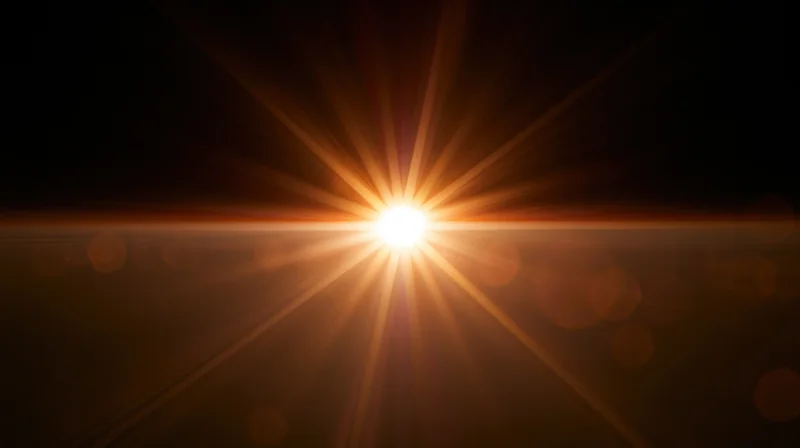 Bright sunburst radiating golden light across dark background with lens flare and bokeh effects