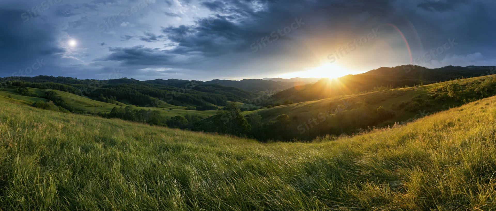 Golden sunlight over rolling green hills and grassy fields at sunset