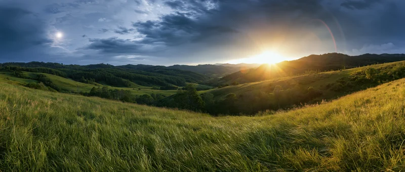 Golden sunlight over rolling green hills and grassy fields at sunset