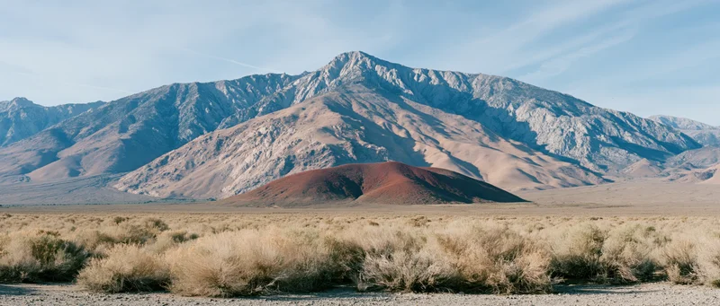 Red volcanic cinder cone in arid desert landscape with distant mountains under blue sky