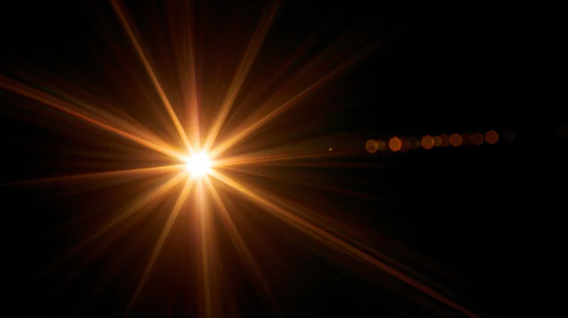 Bright starburst light flare radiating from center against black background with bokeh circles to the side