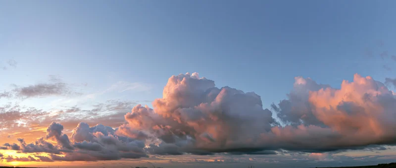 Large cumulus clouds illuminated by sunset light above a distant horizon
