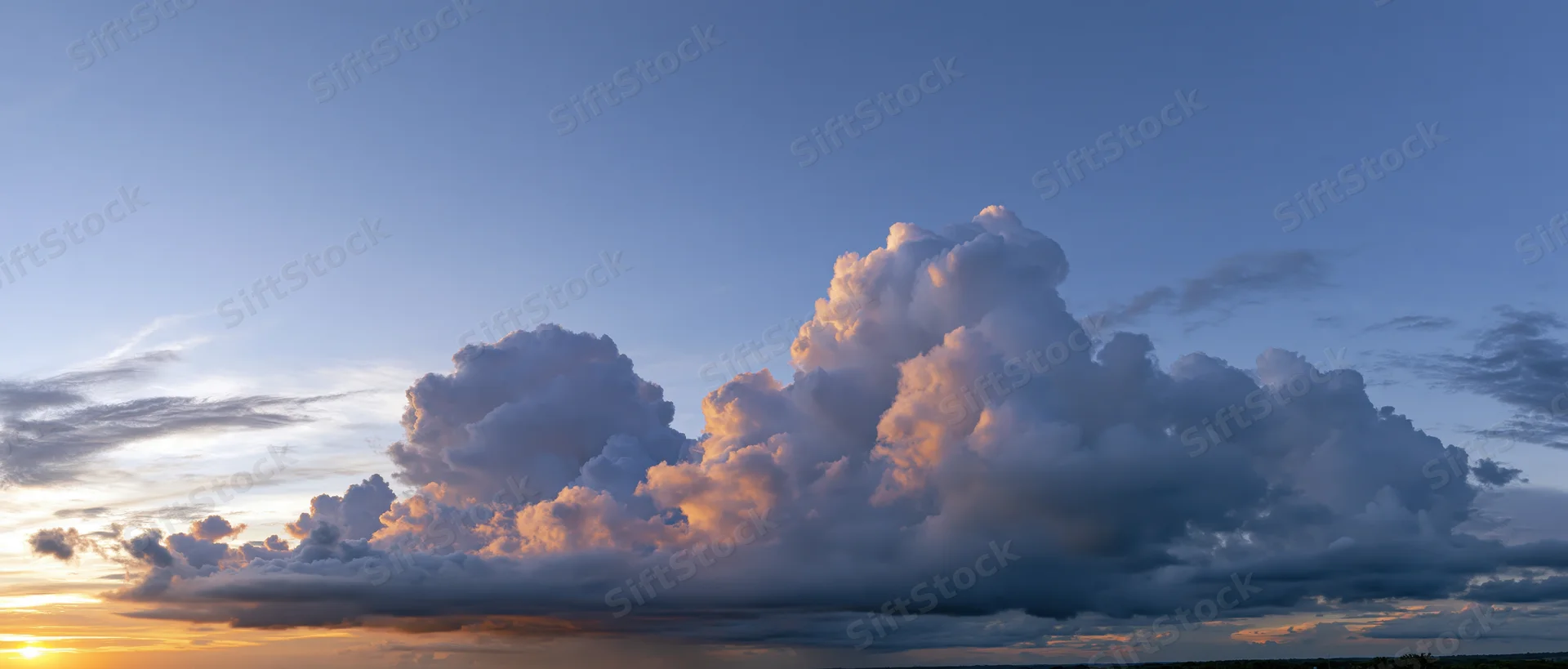 Large cumulonimbus cloud formation at sunset over horizon