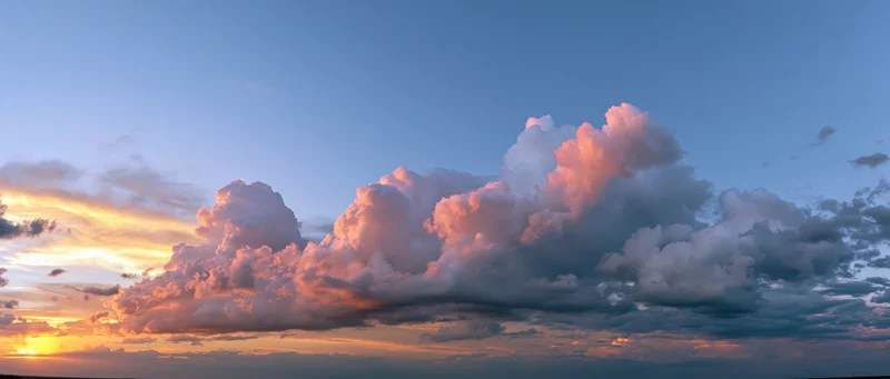 Large cumulonimbus clouds glowing pink and orange at sunset against a blue sky with copyspace above the horizon