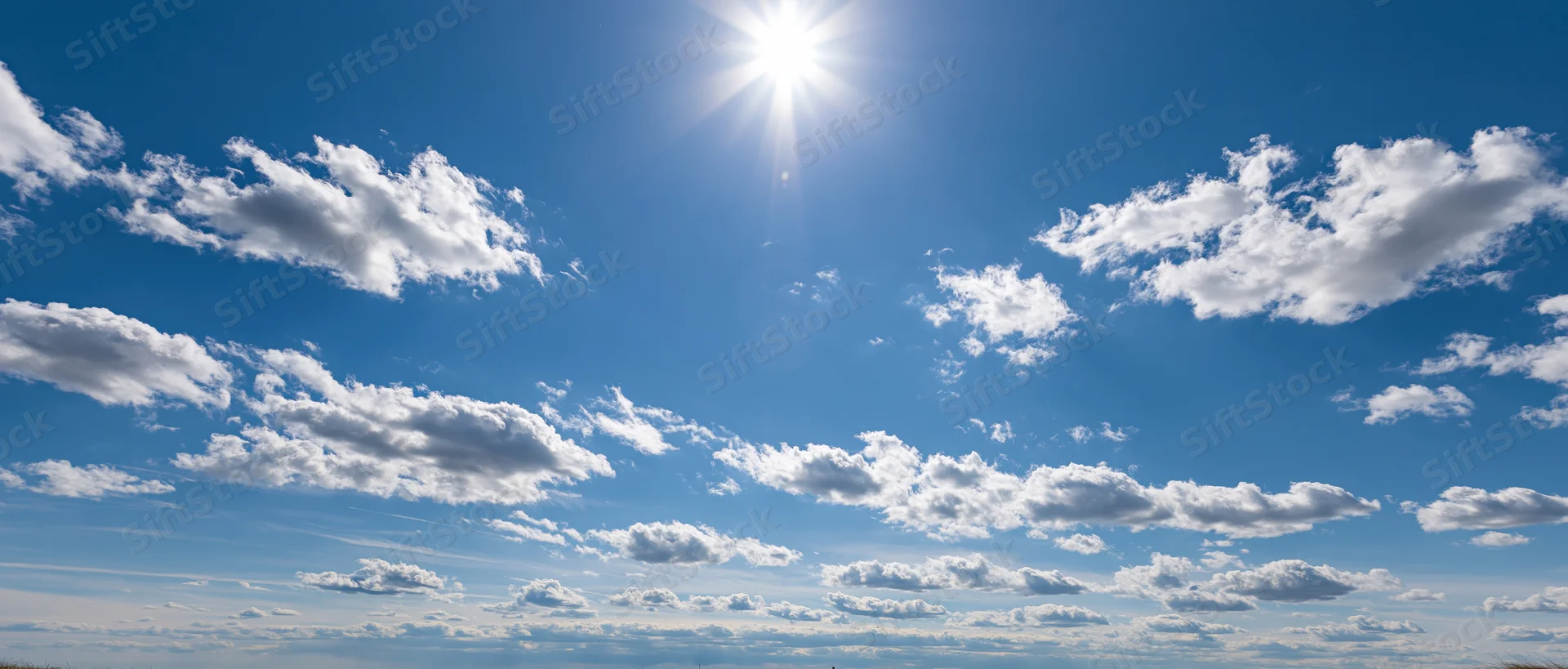 Bright sun shining in a blue sky with scattered white clouds above a distant horizon