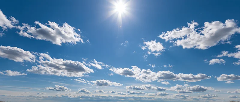 Bright sun shining in a blue sky with scattered white clouds above a distant horizon