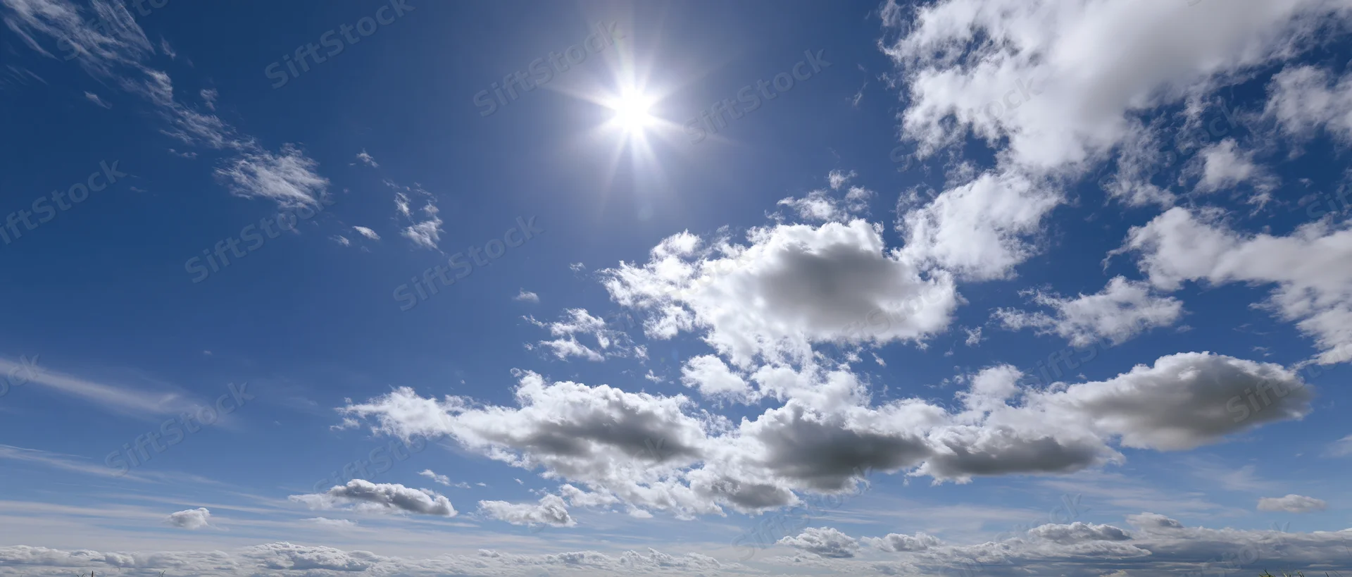 Bright sun shining in a blue sky with scattered white clouds above the horizon