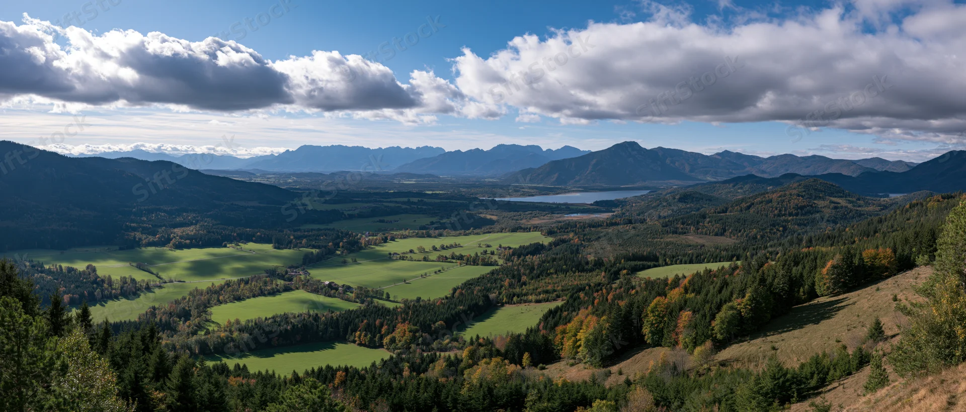 Panoramic view of a mountainous valley with green meadows and autumn forest under a cloudy sky