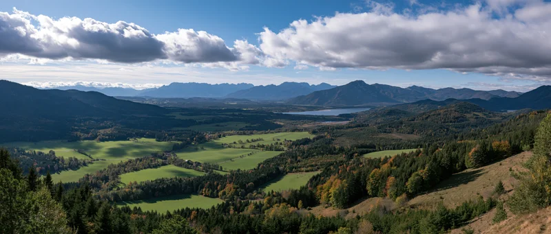 Panoramic view of a mountainous valley with green meadows and autumn forest under a cloudy sky
