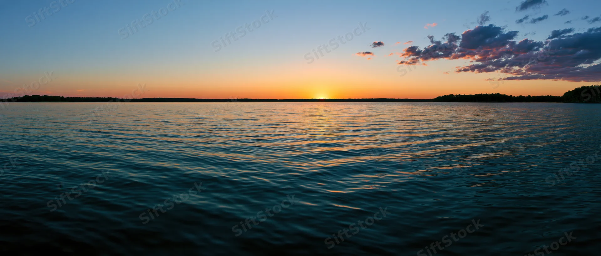 Sunset over calm lake reflecting orange and blue sky at dusk