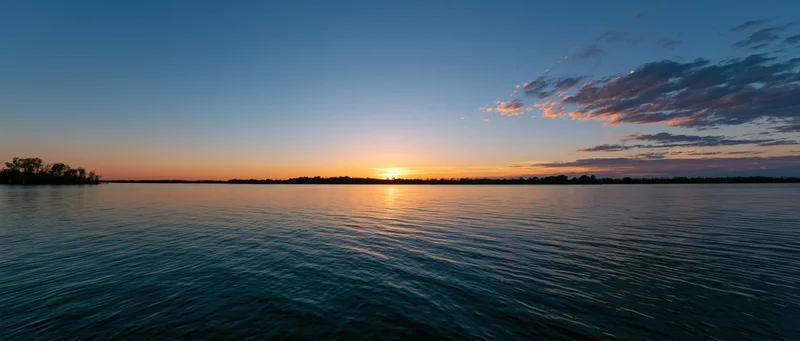 Sunset reflecting on calm lake water at dusk with distant tree-lined shore