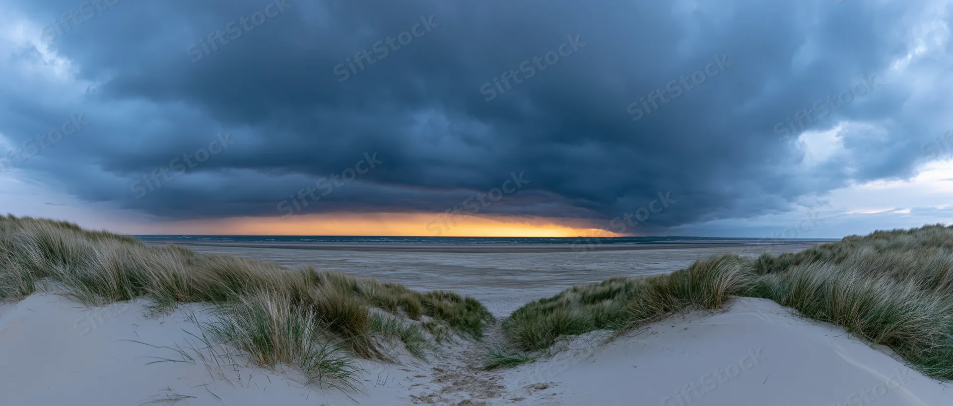 Storm clouds over a sandy beach with dunes and grass at sunset