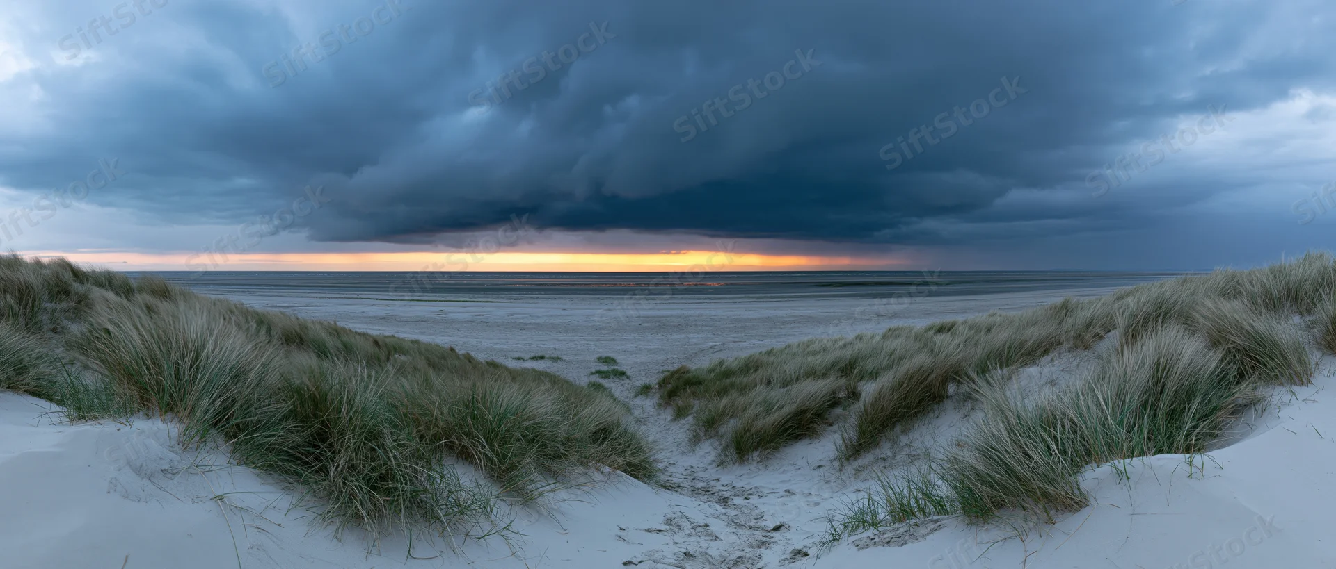 Storm clouds over a sandy beach with dunes and marram grass at sunset