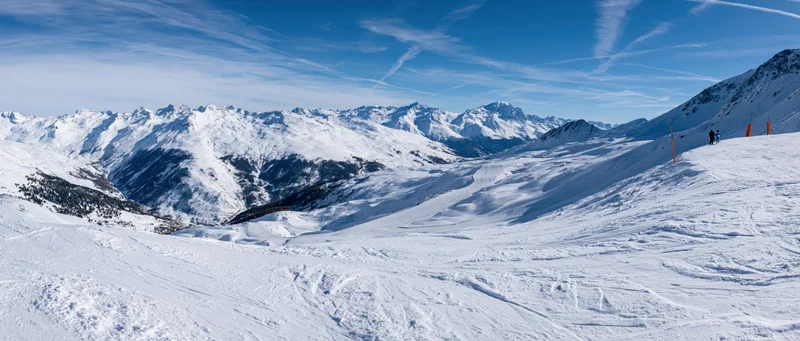 Snow-covered alpine mountains with ski slopes and distant skiers under a clear blue sky