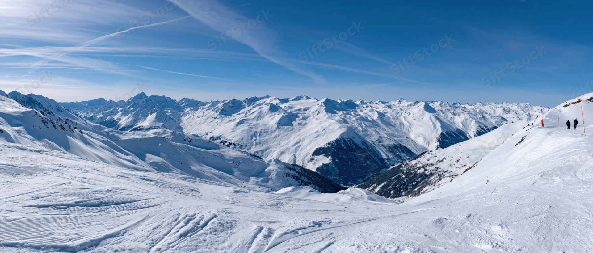 Snow-covered alpine mountains with ski slopes and distant skiers under a clear blue sky