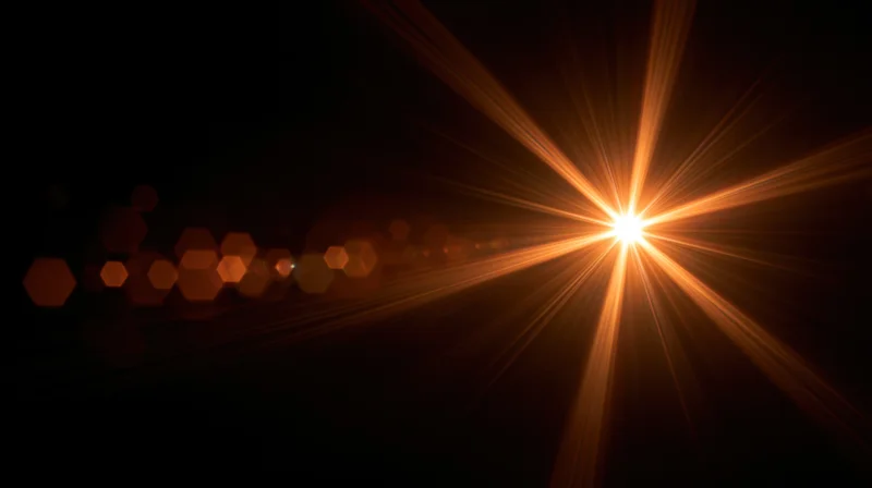 Bright orange starburst light flare with hexagonal bokeh against dark background