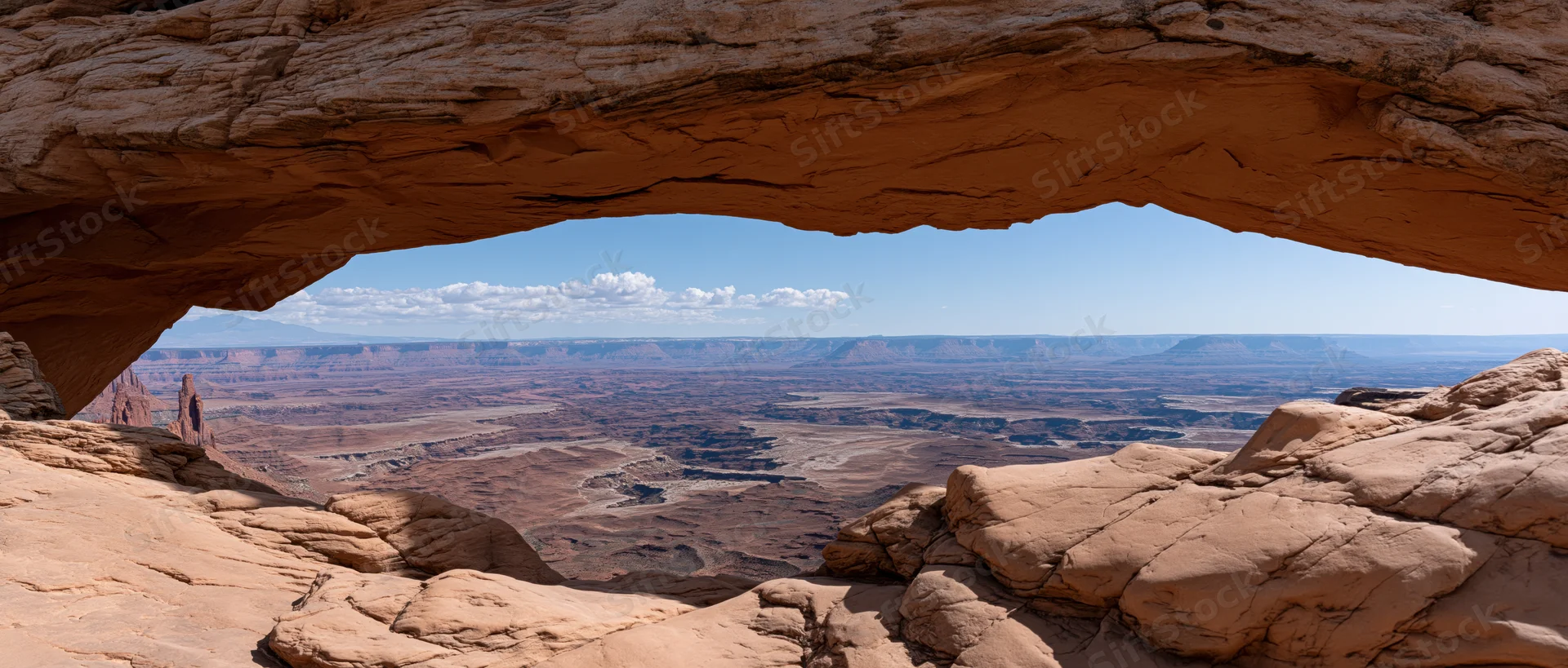 View through a natural rock arch overlooking a vast desert canyon landscape
