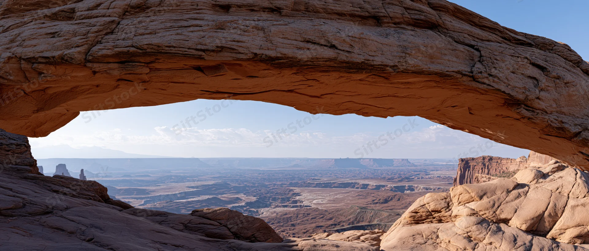Natural rock arch framing a desert canyon landscape with distant buttes and mesas under a blue sky