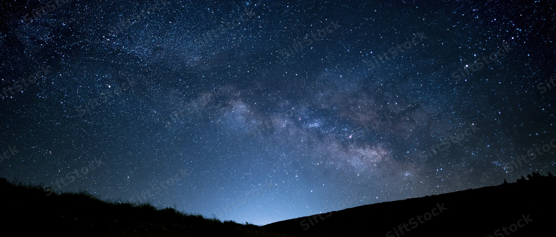 Milky way galaxy stretching across dark night sky above silhouetted hills