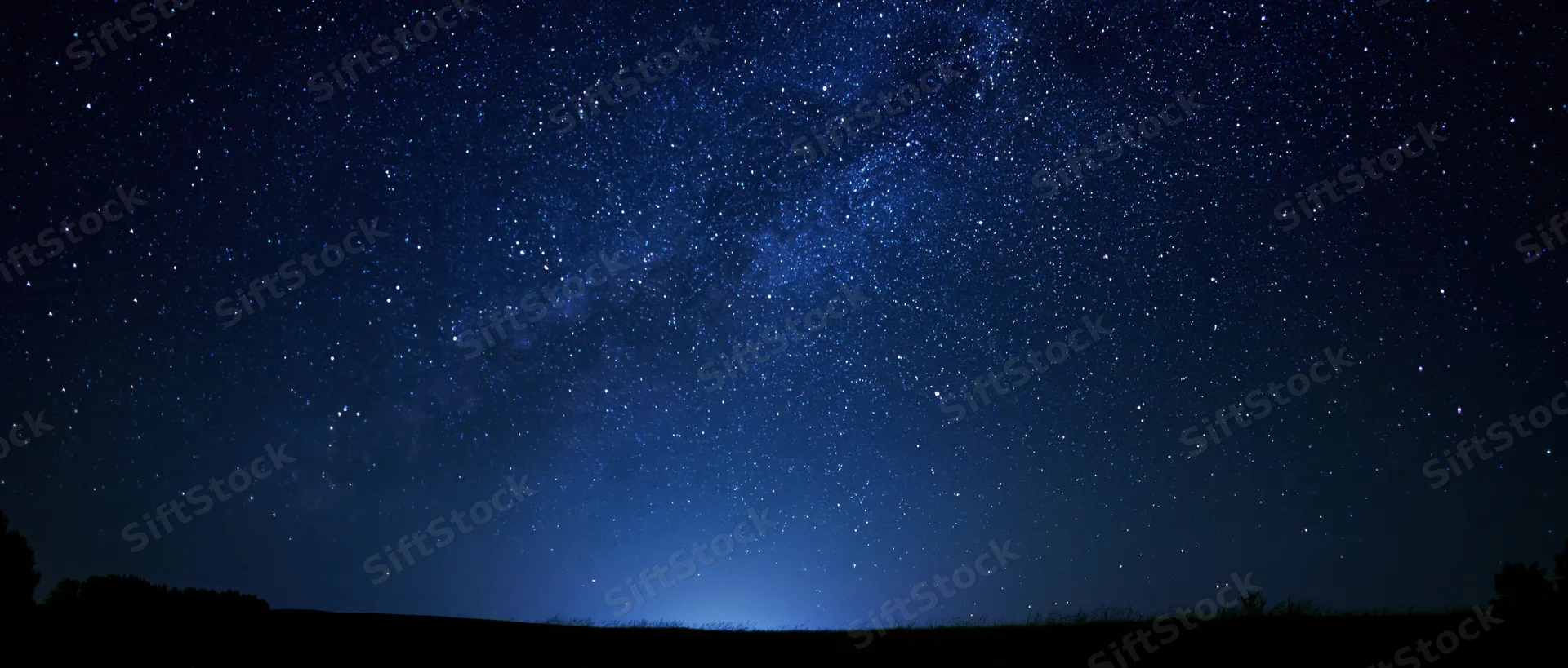 Milky way galaxy stretching across dark night sky above rural horizon