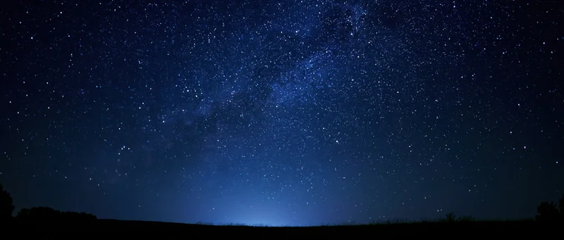 Milky way galaxy stretching across dark night sky above rural horizon