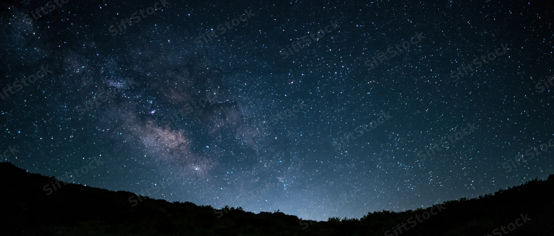 Milky way galaxy visible across night sky above dark mountain silhouette