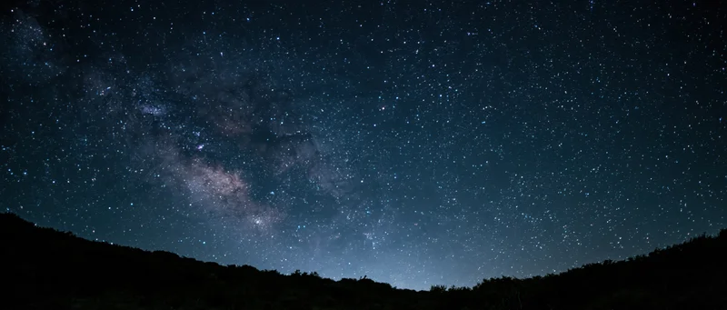 Milky way galaxy visible across night sky above dark mountain silhouette