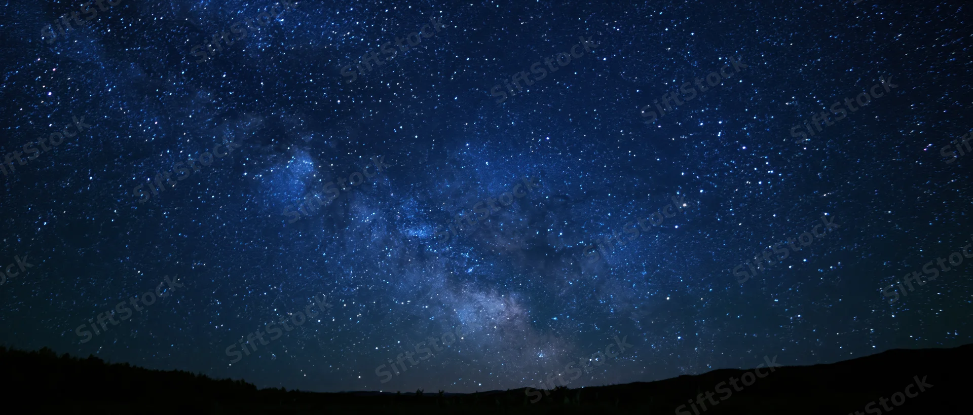 Milky way galaxy stretching across dark night sky above forested horizon