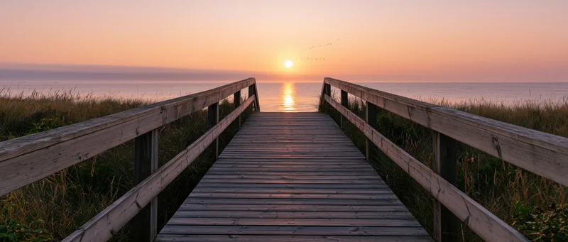 Wooden boardwalk leading to ocean at sunset over dunes