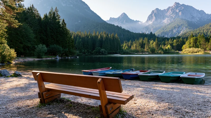 Wooden bench facing calm lake with colorful rowboats and forested mountains in background