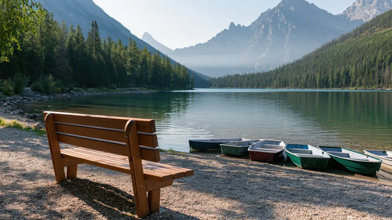 Wooden bench on gravel shore beside calm lake with boats and forested mountains in background
