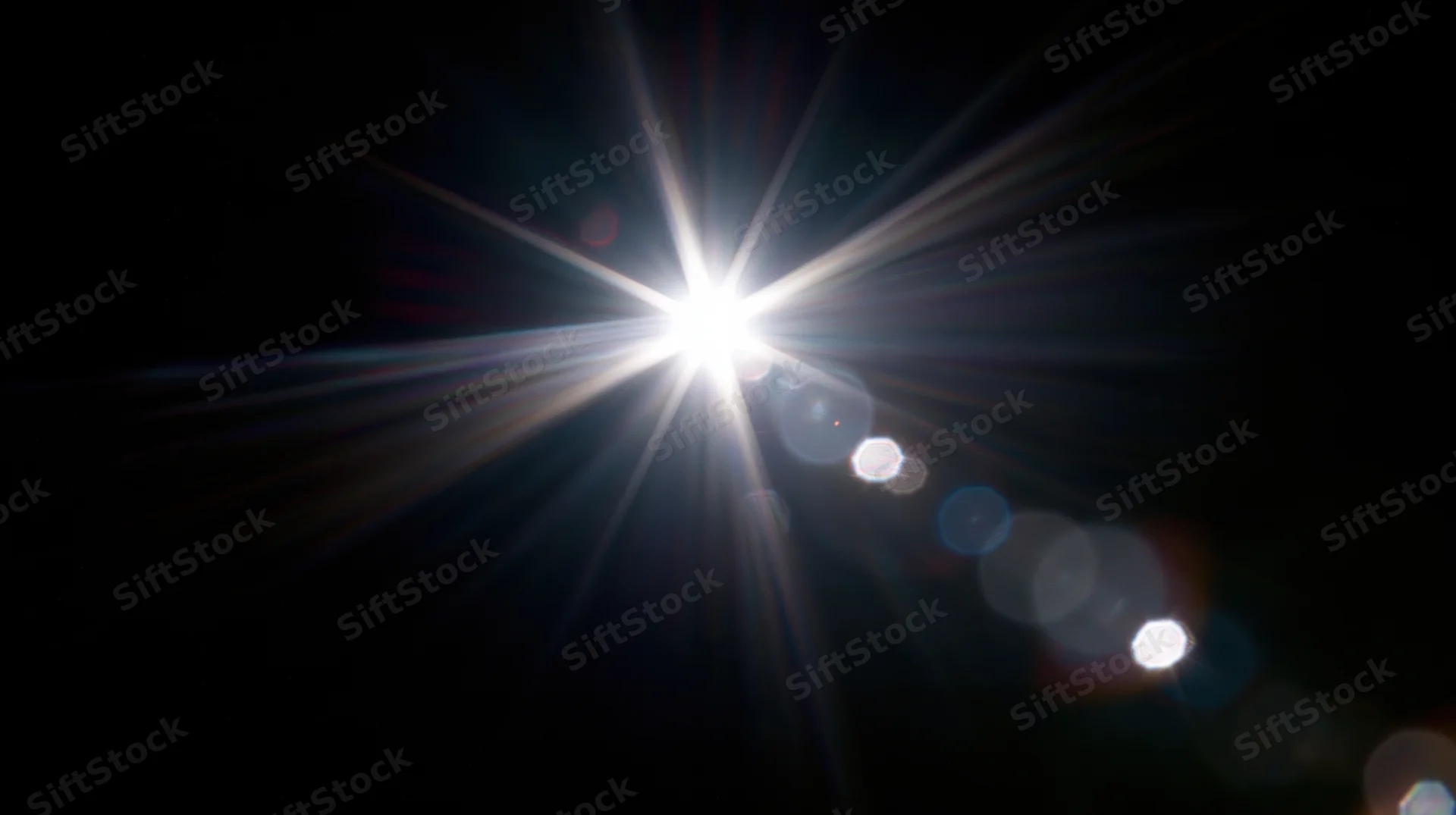 Bright light source emitting starburst rays and bokeh highlights against dark background