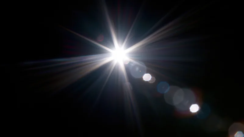 Bright light source emitting starburst rays and bokeh highlights against dark background