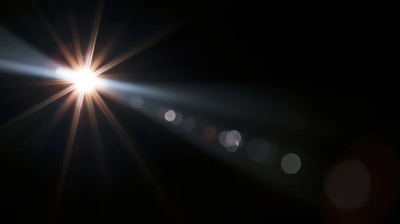 Bright light source creating starburst flare and bokeh circles against dark background