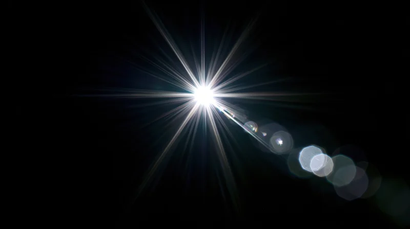 Bright starburst light flare with bokeh circles on black background