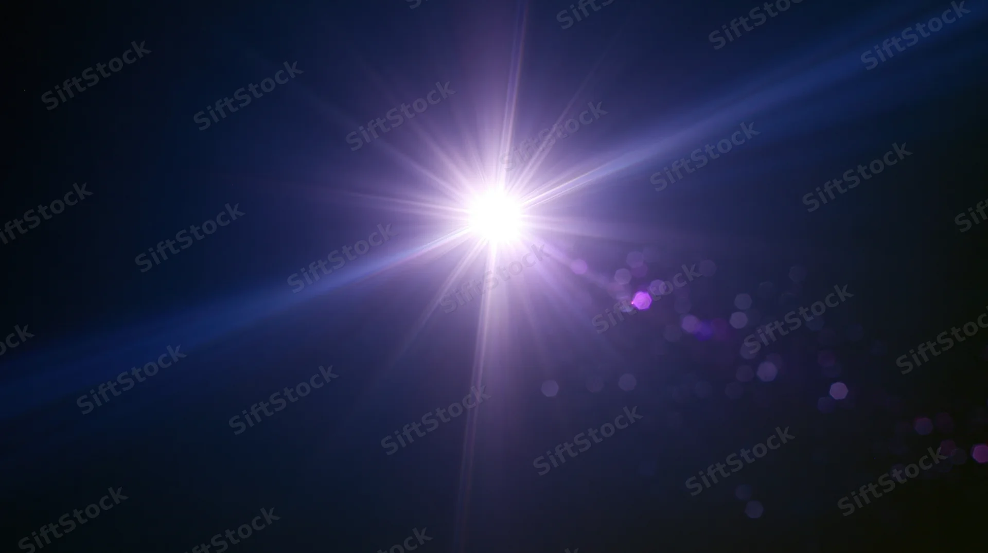 Bright starburst light radiating in dark blue sky with purple bokeh and lens flare effects